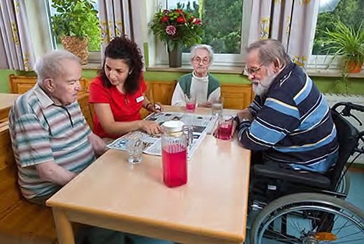 Das Bild zeigt eine Mitarbeiterin, die mit den Bewohnern Zeitung liest