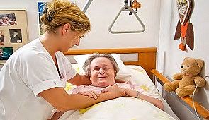 Das Bild zeigt eine Pflegekraft mit einer Bewohnerin, die im Bett liegt