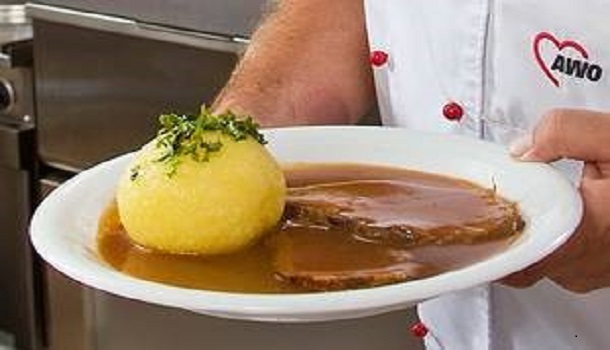 Das Bild zeigt einen Knödel mit Braten, das von einer Hand gehalten wird.